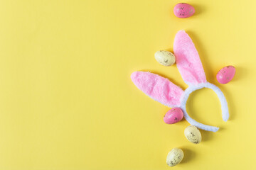 Costume bunny ears and Easter eggs top view on yellow background.