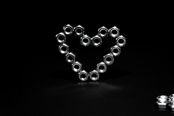 Heart shape made of hex bolts on black background. Creative love concept
