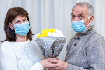 Couple seniors celebrate Valentine's Day in mask. Man gives woman a favorite bouquet of flowers....