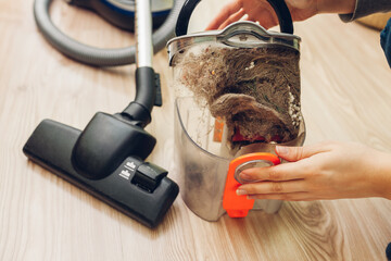 Woman opening dust filter out of vacuum cleaner at home. Hoover container full of dirt and cat's...