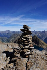Nahaufnahme eines Steinm&auml;nnchens, im Hintergrund ein Gipfelpanorama