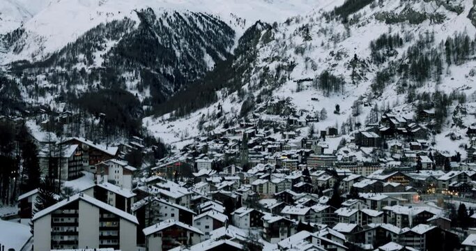 Cityscape of the Swiss village of Zermatt in Valais in winter, at dawn with snow and illuminations. The Matterhorn and the Alpine mountain range in the background.