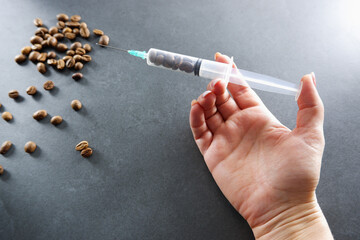 Grains of coffee and an injection syringe in female hands. Caffeine addiction concept.