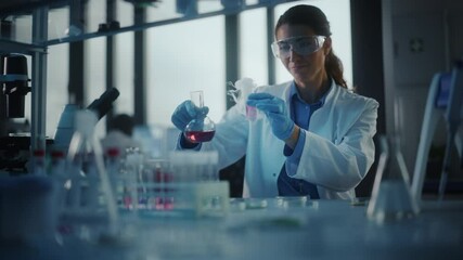 Beautiful Female Scientist Wearing Protective Goggles Mixing Chemicals in a Test Tube in a Lab