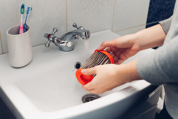 Cleaning vacuum cleaner filter. Woman washing hoover filter with water in bathroom sink at home. Hosehold chores