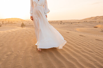 Fototapeta na wymiar Young barefoot woman in bridal dress walking on sand dune in desert.