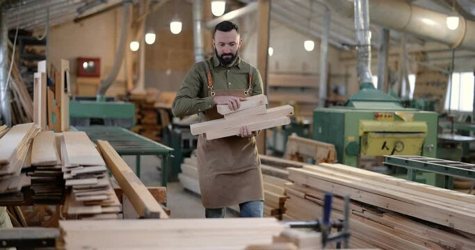 Carpentry worker carrying planks for some woodwork at the manufacturing. Handsome man working with wood at the joinery
