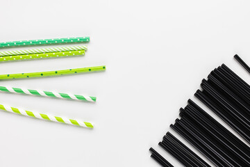 Many black plastic and green eco friendly paper straws on white background. Recycle, environment conversation, pollution and plastic straw ban concept. Copy space