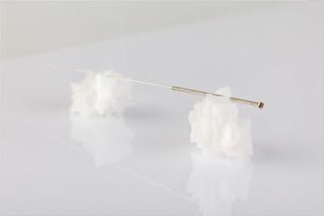 Silver needles for traditional Chinese medicine acupuncture rest on salt crystals. Close-up. White background.