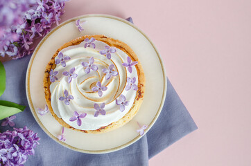 top view french dessert with lilac flowers. lemon tartlet with italian meringue, whipped cream on pink background with copy space, place for text. creative decoration.