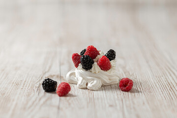 Merengue cake, decorated with raspberries and blackberries. Pavlova cake. Light wooden background. Home cooking.