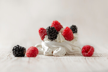 Homemade delicious Pavlova meringue cake with fresh raspberries and blackberries on a wooden background. Close-up. Copy space.