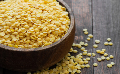 Uncooked raw yellow lentil in bowl on wooden background, (Lens culinaris)