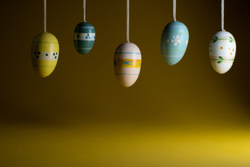 Happy Easter greeting card background with empty copy space. Colorful Easter eggs hanging over yellow background.