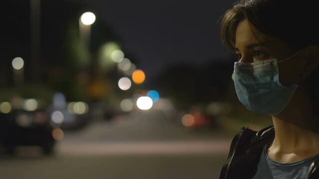 pandemic, 2021 - serious woman pulls down her mask to breathe - city night