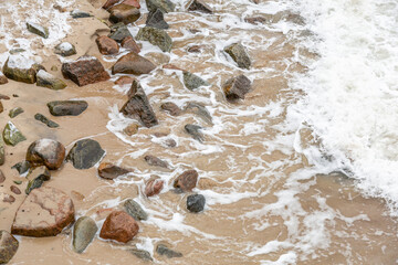 Natural large stones and sea waves on a sandy beach