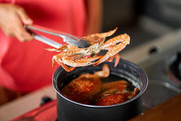Taking out cooked blue crab from pot with boiling water