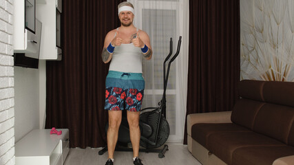 Fototapeta na wymiar Gray-haired Caucasian retro-styled sportsman guy showing thumbs up, smiling before hard training at home. Fit muscular man in funny clothes running, working out, making sport fitness exercises