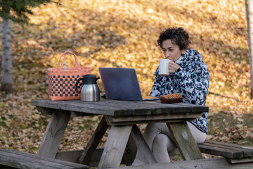 Freelance woman drinking coffee is working with laptop in the park. working outside