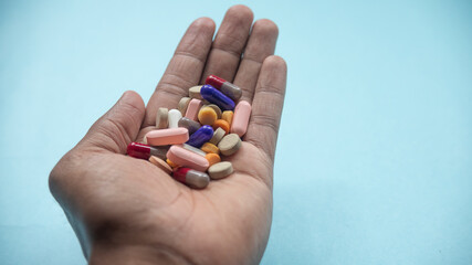 MALE HAND WITH BROWN SKIN, HOLDING PILLS WITH BLUE BACKGROUND AND NATURAL LIGHT.