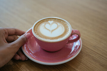 Cup of coffee standing on wooden table. Close up hand holding cup of aroma cappuccino in cafe