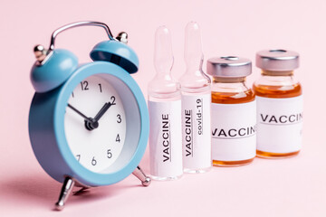abstract vaccine vials and bottles for injection over pink background. alarm clock near vaccination...