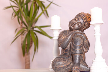 Estatua de un buda entre dos velas blancas y una palmera.