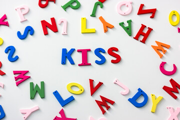 Kiss - a word of multicolored letters on a white table background, English or American Flat Lay alphabet. Valentine's Day.