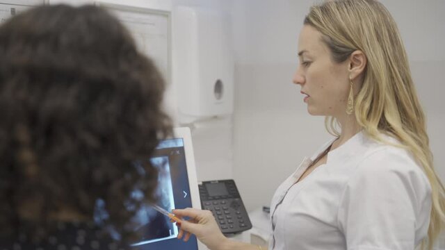 Female orthodontist or dentist explaining a procedure while pointing at a teeth Panoramic Dental X-ray. Young doctor in clinic shows dental radiography before teeth straightening treatment