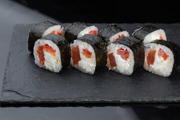 Close-up of uramaki sushi rolls with red caviar, salmon, tuna, cucumber and avocado isolated on black background. Delicious traditional japanese food with sushi rolls.