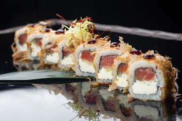 Macro shot of eating uramaki sushi rolls with cream cheese, fried salmon, tuna shavings or dried bonito, cucumber, nori. Chopsticks holding fresh katsuobushi roll in Japanese restaurant closeup