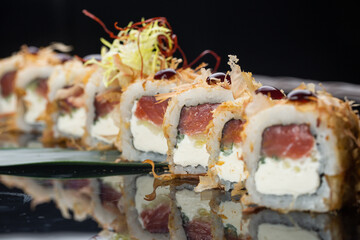 Macro shot of eating uramaki sushi rolls with cream cheese, fried salmon, tuna shavings or dried bonito, cucumber, nori. Chopsticks holding fresh katsuobushi roll in Japanese restaurant closeup