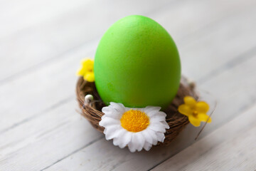 Painted Easter egg in a basket on a light wooden background, top view