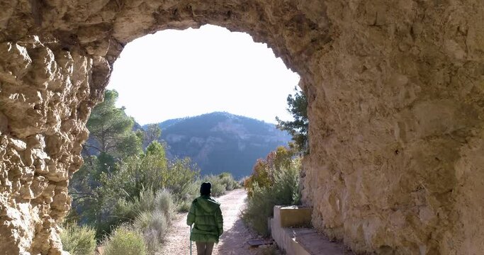 mujer con abrigo plumas sale a valle desde gruta de piedra y dron la sigue detr&aacute;s