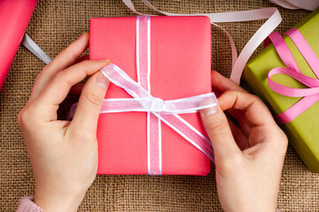 Gift wrapping process. The girl is packing a pink gift with a white ribbon.