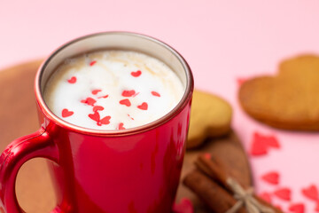 Red latte cup with heart shaped cookies, cinnamon, anise and red hearts on pink background