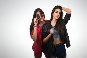 Young twins. Teen twin sisters wearing leather jackets and sunglasses on light background