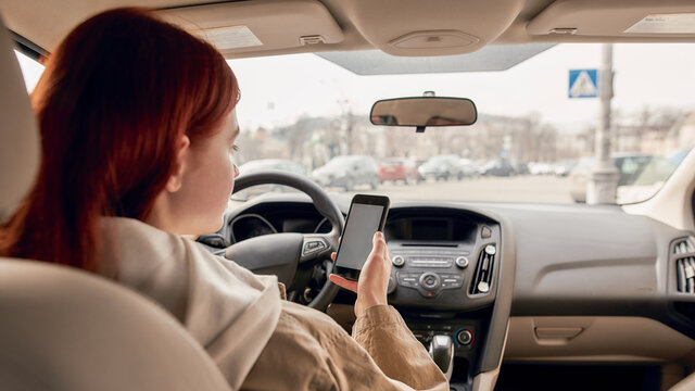 Distracted young female driver looking at the screen of her mobile phone while driving a car. Technology and transportation concept