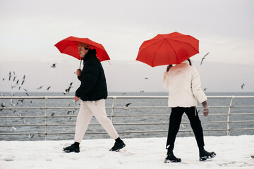 Young hipster couple walking with two red umbrellas in cold weather, love story outdoors