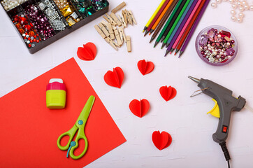 On a light background, colored pencils, wooden clothespins, pebbles, scissors, paper, glue, grater, oil gun, patterns of hearts. Decor hearts.Step by step instructions.Do it yourself.Red heart