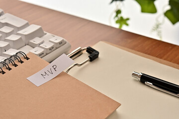 A sticky note labeled MVP is taped to the edge of a notebook on the desk.That's an acronym for Minimum Viable Product.