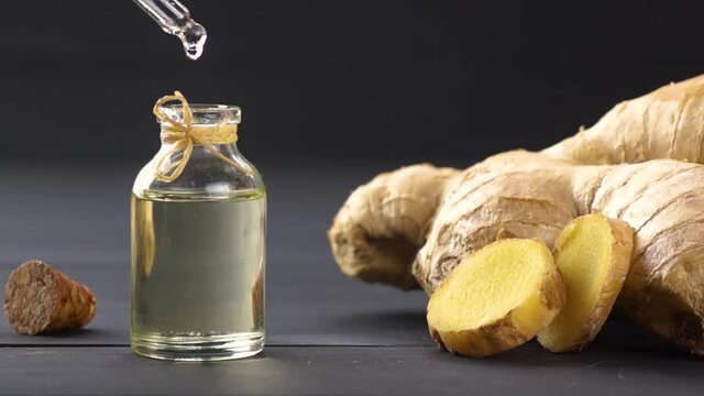 Glass bottle of essential ginger oil, ginger root and powder on black wooden rustic background, oil dripping, Zingiber officinale