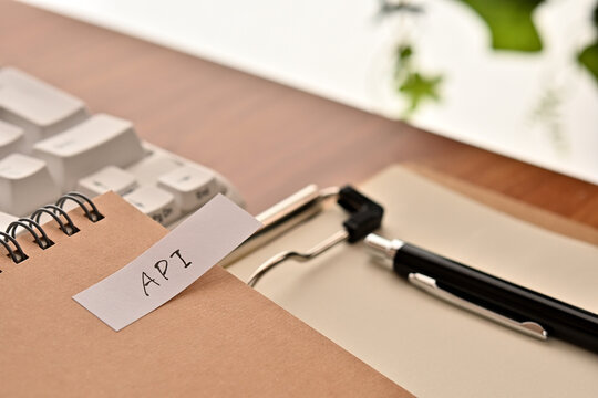 A sticky note labeled API is taped to the edge of a notebook on the desk.That's an acronym for Application Programming Interface.