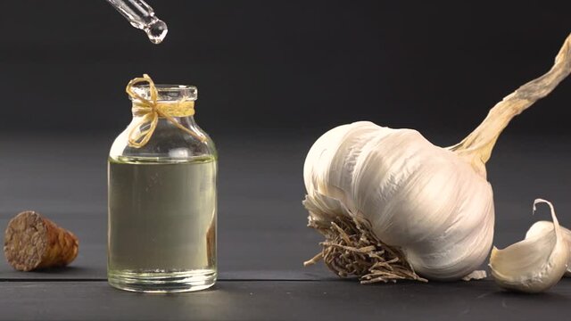 Ripe and raw garlic and garlic oil in glass of bottle on black wooden table, oil dripping