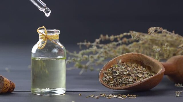 Glass bottle of thyme essential oil and bunch of dry thyme on black wooden rustic background, oil dripping