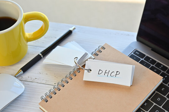 There's a word book on a desk with a cup of coffee and laptop pc. The word DHCP is written in it. It's an abbreviation for Dynamic Host Configuration Protocol.