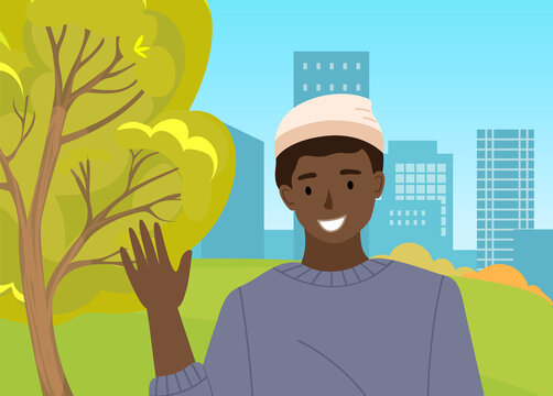 Handsome boy is waving hand. Male character is showing greeting gesture on the background of cityscape. Cheerful man is raising his hand in the open area against with green trees summer day