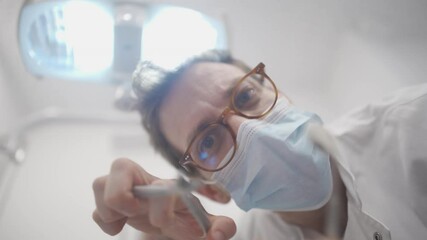 Point of view of white male dentist using a dental bone rongeur before preforming a tooth extraction procedure on patient. Doctor looking down and examining patient during complicated procedure