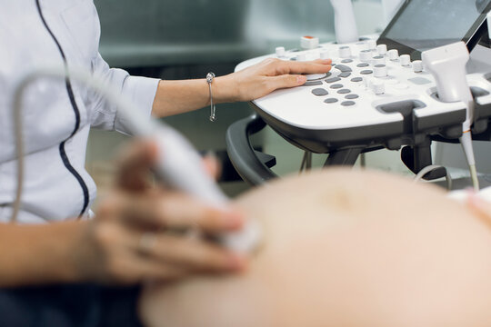 Close up cropped image of female doctor obstetrician, pushing buttons on a control panel performing ultrasound sonogram procedure for pregnant woman