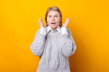Photo of surprised young woman gesturing over yellow background.